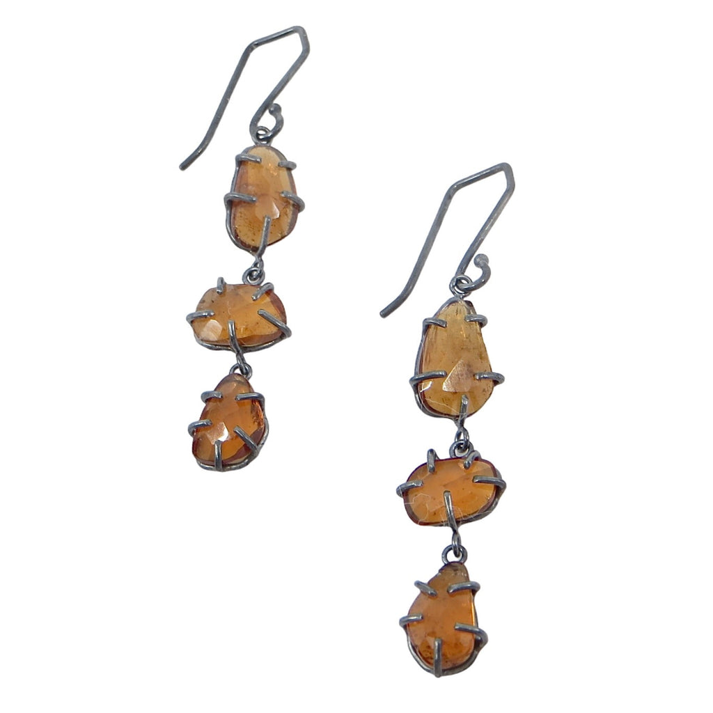 Three hessonite garnets on each earring dangle in oxidized silver prong settings. The rose cut geometrics gems dangle from geometric shaped ear wires. Edgy elegance of golden garnets in contrasting black settings. 2" long.