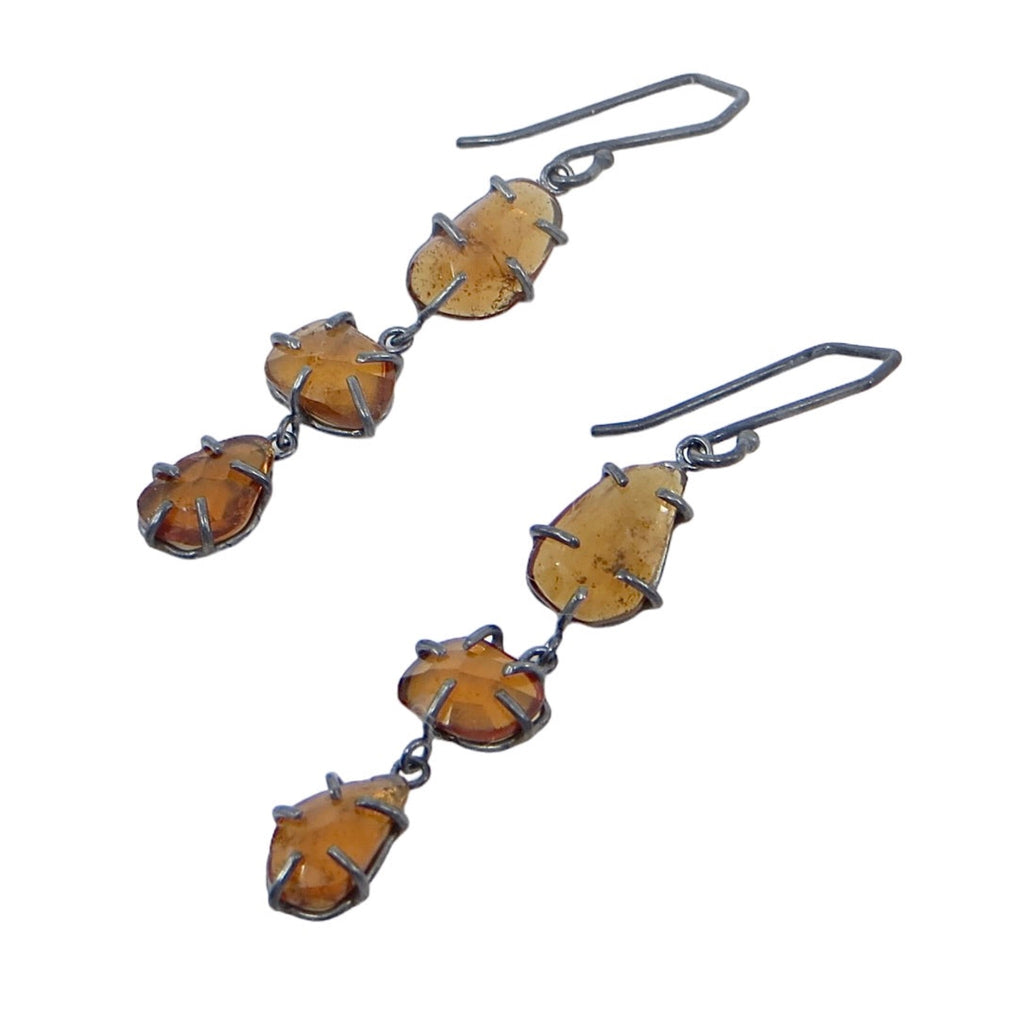 Three hessonite garnets on each earring dangle in oxidized silver prong settings. The rose cut geometrics gems dangle from geometric shaped ear wires. Edgy elegance of golden garnets in contrasting black settings. 2" long.