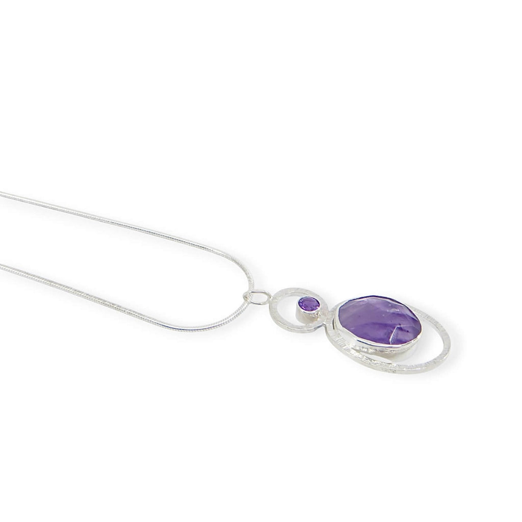 Bezel set rose cut oval atomic amethyst and tube set round faceted amethyst. Each in a textured sterling frame to make a single pendant. Suspended from 16" sterling snake chain.