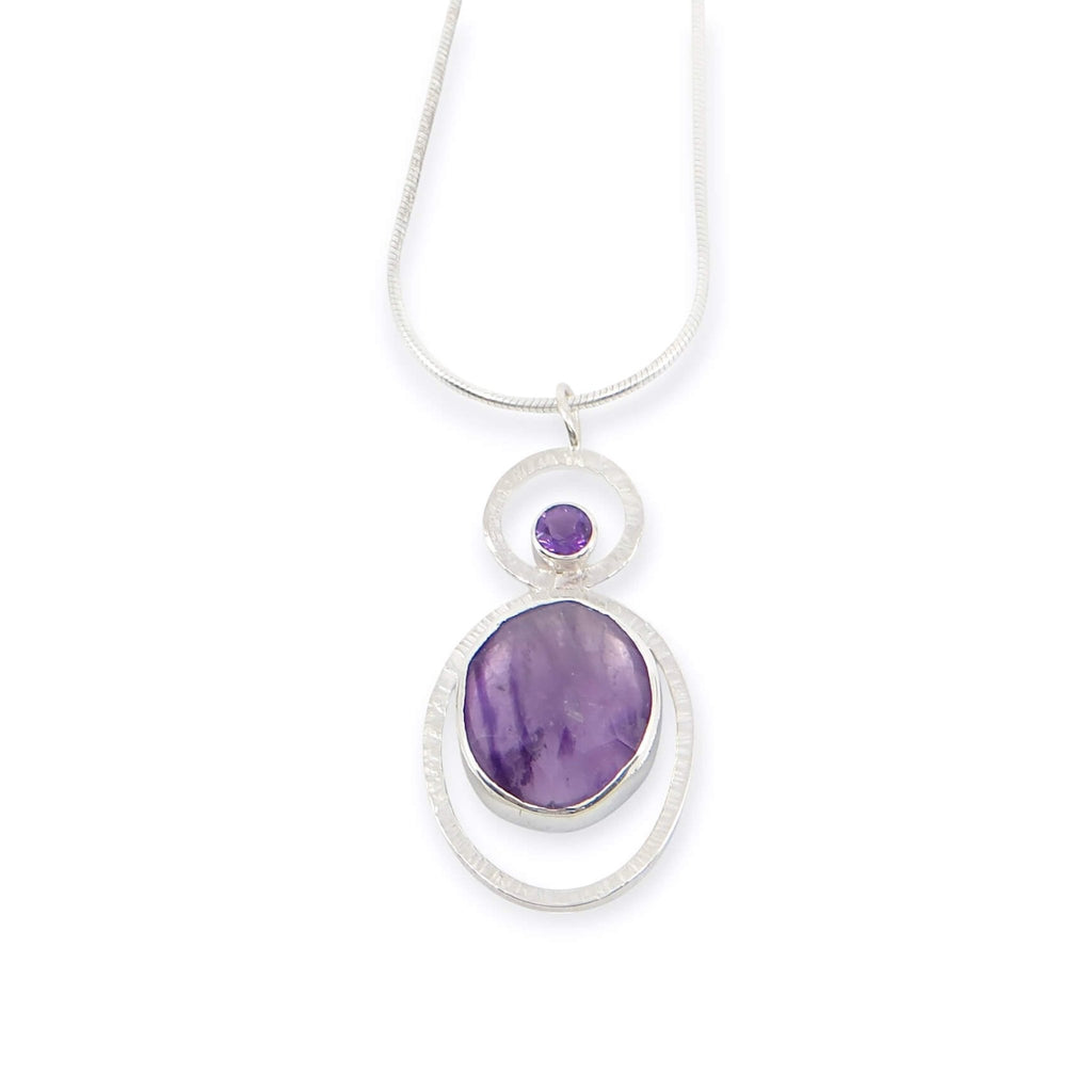 Bezel set rose cut oval atomic amethyst and tube set round faceted amethyst. Each in a textured sterling frame to make a single pendant. Suspended from 16" sterling snake chain.