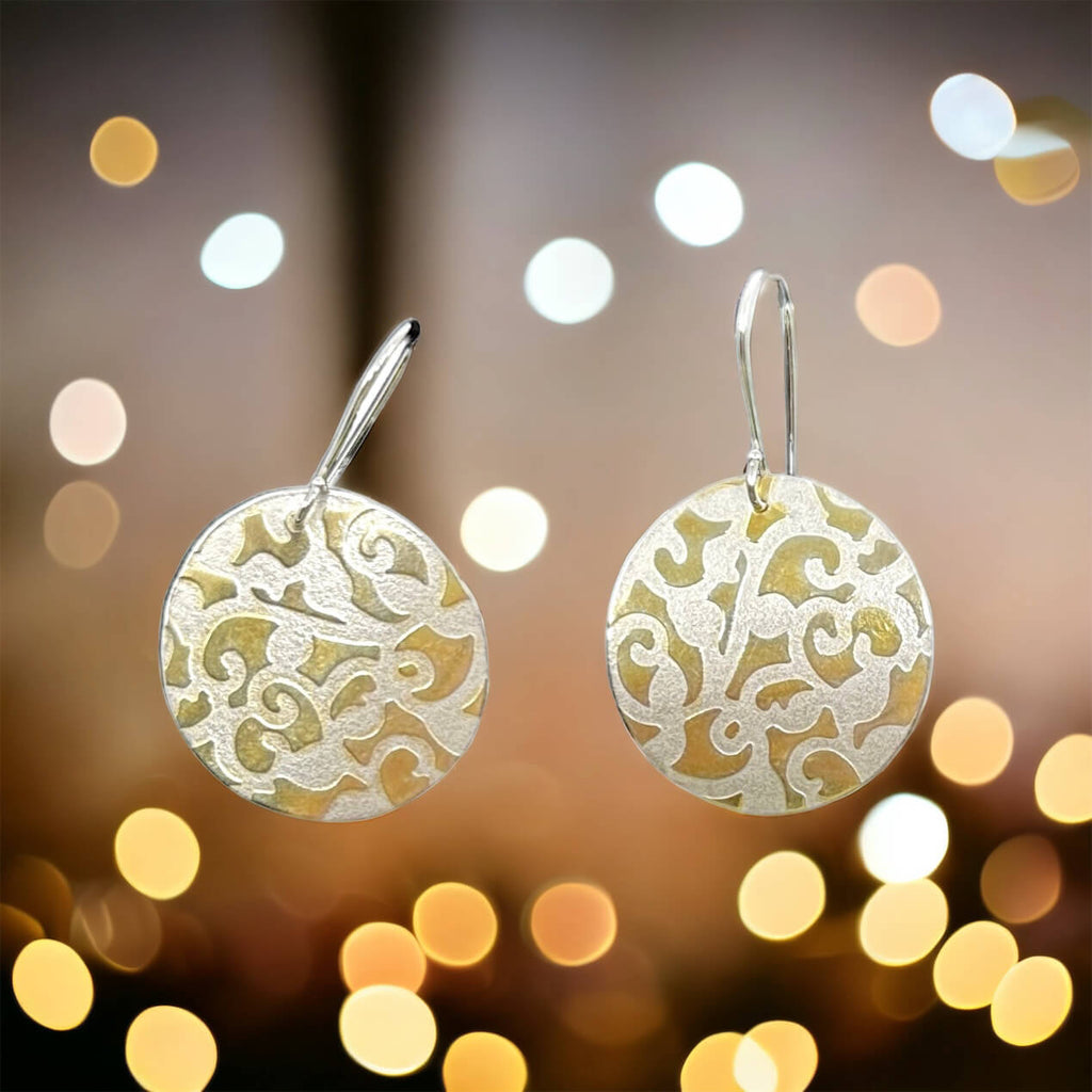Earrings. Slightly domed 1" textured sterling discs with puzzle piece-like cutout patterns have textured sterling silver recesses and high polish 18k gold high points. They flutter from argentium silver ear wires.