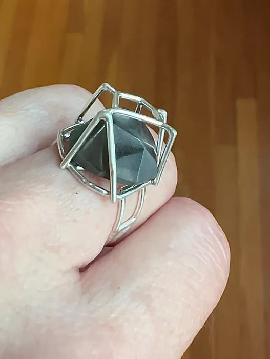 Video of ring on finger and stone moving. Angular geodesic-like cut hematite moves  around inside a sterling silver cage setting. Angular band--all linked wires--complements the setting and stone angles. US size 7.