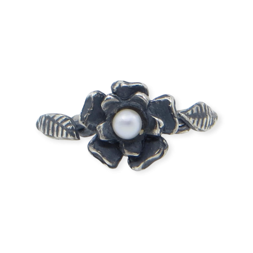 Two layers of different size flower curve upwards surrounding a sweet white pearl. A twisted wire ring band featured carved leaves on either side of the flower. A black patina provides a contrast to the silver and pearl. US Size 7.25