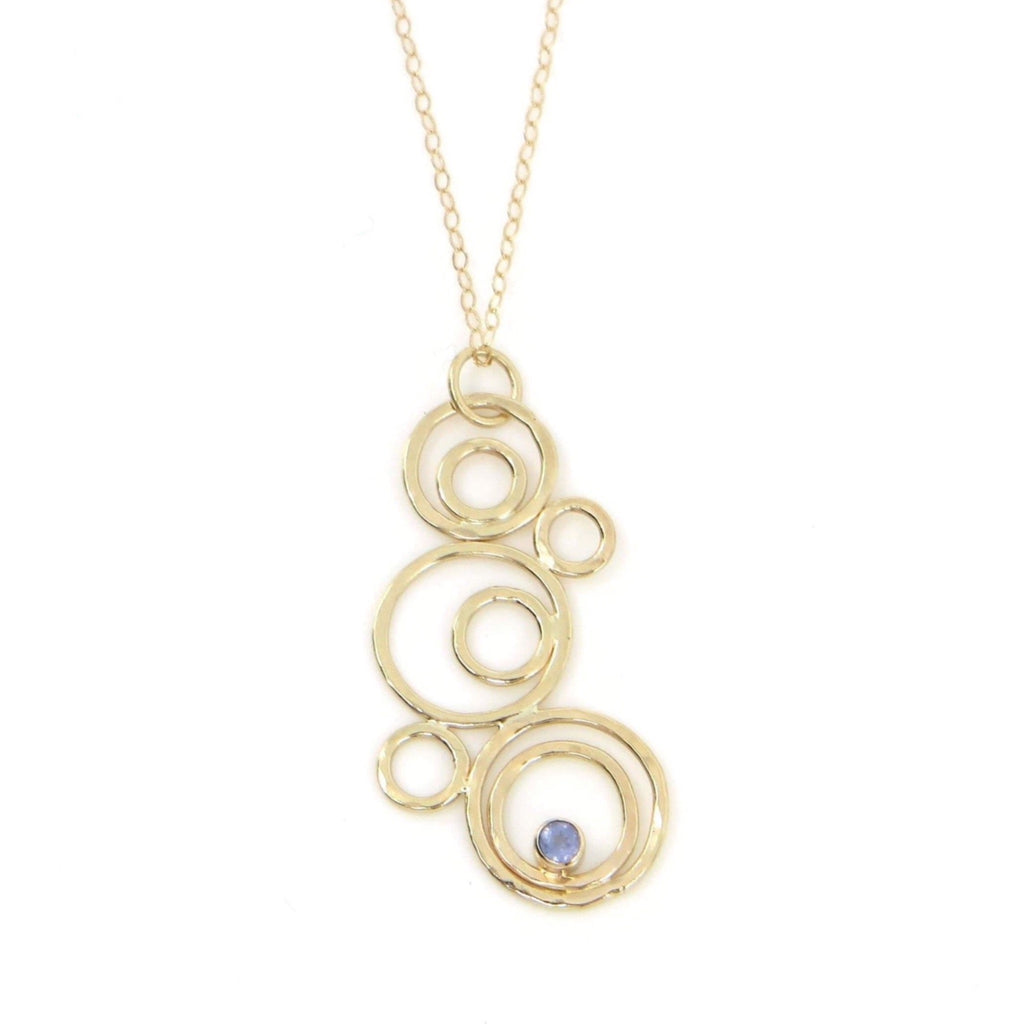 Hammered gold "bubbles" are assembled to create a pendant. A tube set tanzanite floats in one of the bubbles. Pendant is suspended from a 14k gold chain.