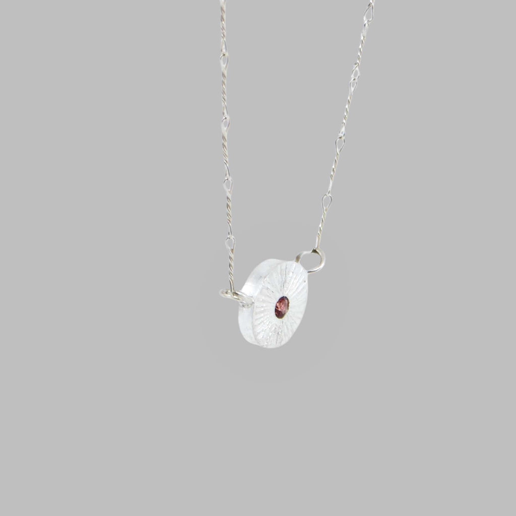 Sweet petite chunky textured disc with flush set center garnet necklace. Delicate twisted link chain suspends the disc from each side. Perfect for all occasions and for January birthdays!